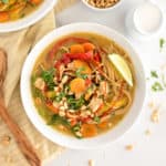 White bowl with thai soup with noodles, peppers, and cilantro