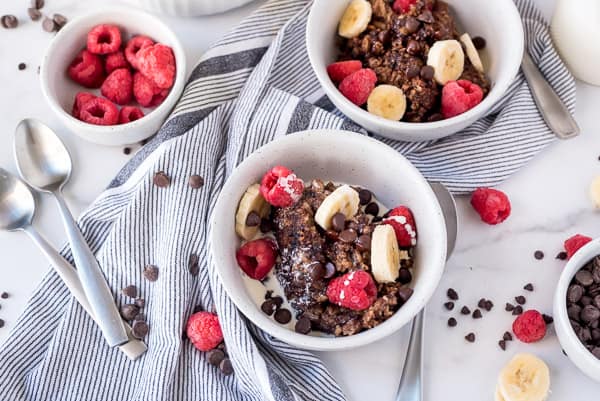 Two white bowls of chocolate oatmeal with bananas and berries