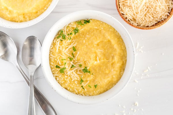 Creamy polenta in a white bowl garnished with herbs and cheese
