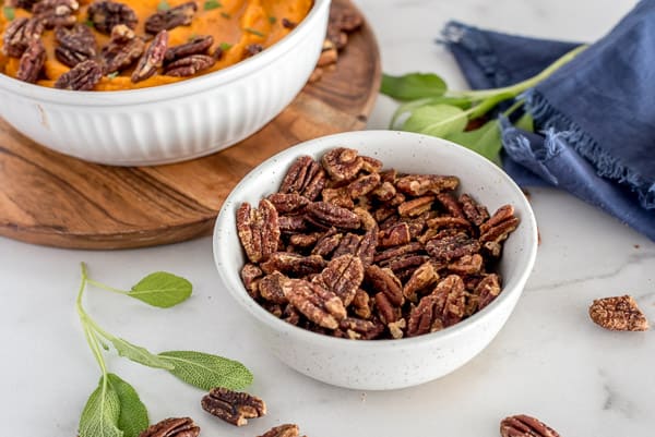 Roasted pecans in a white bowl with sweet potatoes in the background