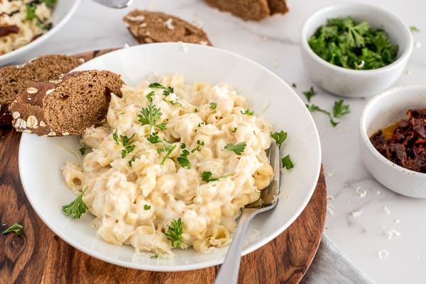cauliflower mac and cheese in a white bowl topped with herbs