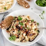 cauliflower mac and cheese in a white bowl topped with sun-dried tomatoes and balsamic glaze