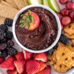 white bowl of chocolate hummus with a side of strawberries, blackberries, pretzels, apples, and graham crackers