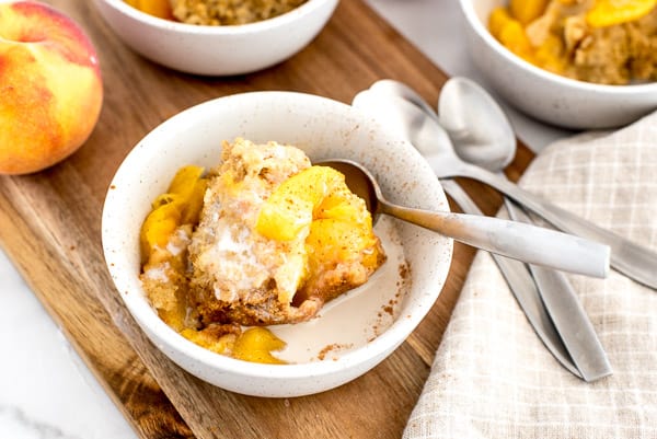 2 white bows with peach cobbler, cream, and a spoon
