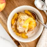 white bowl with peach cobbler, cream, and a spoon