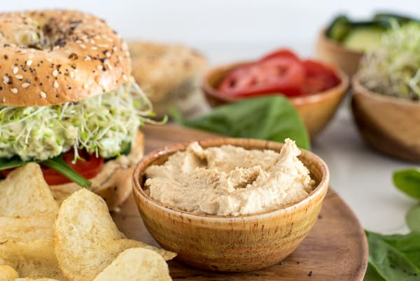 bowl of hummus next to a bagel sandwich