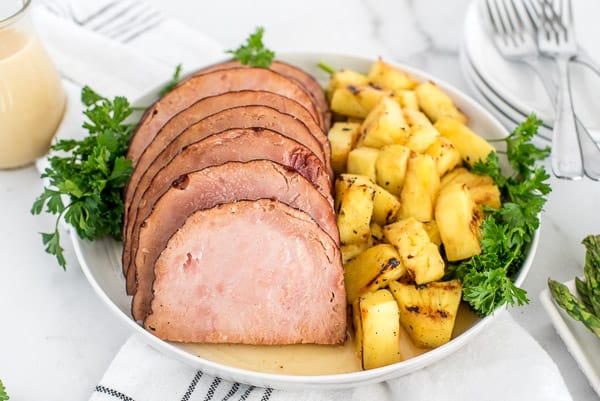 Ham on a white plate with pineapple and herbs