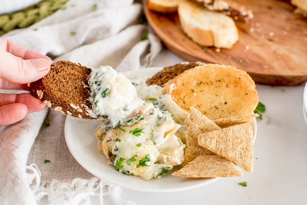 healthy spinach artichoke dip in a white bowl served with bread and chips