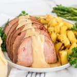 Ham on a white plate with mustard sauce, pineapple and herbs