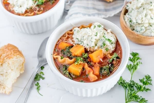 instant pot lasagna soup with a cheese topping in a white bowl near a loaf of crusty bread
