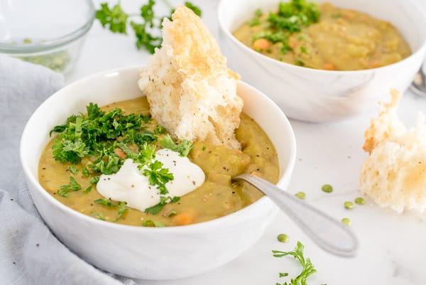 Split pea soup in a white bowl garnished with parsley and sour cream and bread
