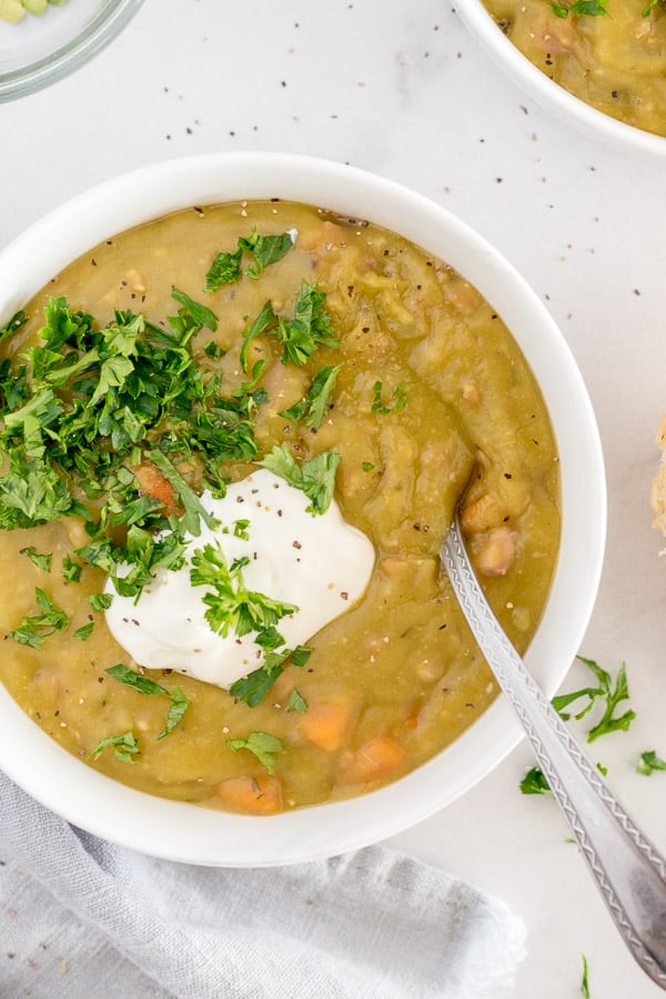 split pea soup in a white bowl garnished with sour cream and herbs