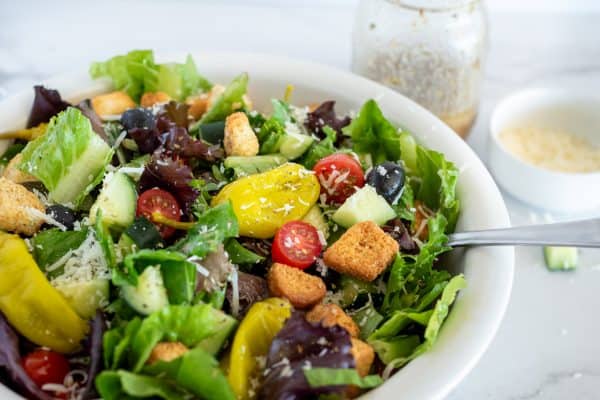Italian salad with cucumber, tomatoes, peppers, and croutons in a white bowl.