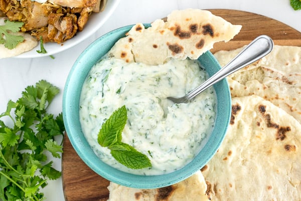 Blue bowl with raita, a piece of naan and a spoon.