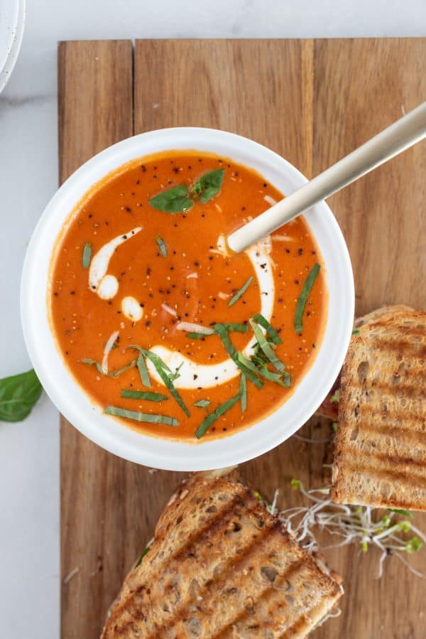 Tomato soup with cream and basil in a white bowl on a wood board