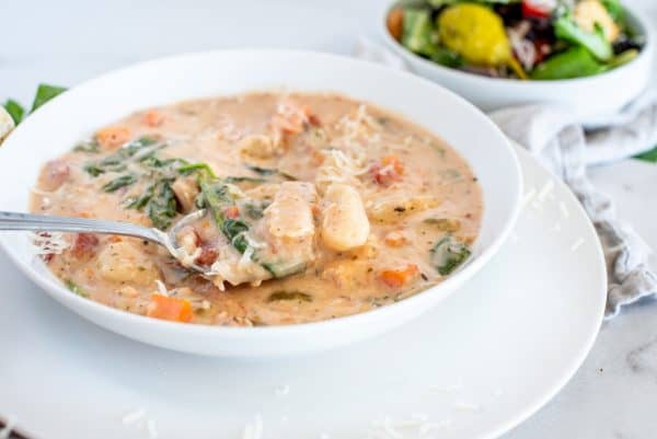 Chicken and gnocchi soup in a white bowl with a salad