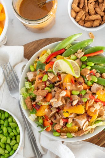 Asian chicken salad with bell peppers, chicken, oranges, and pea pods in a white bowl