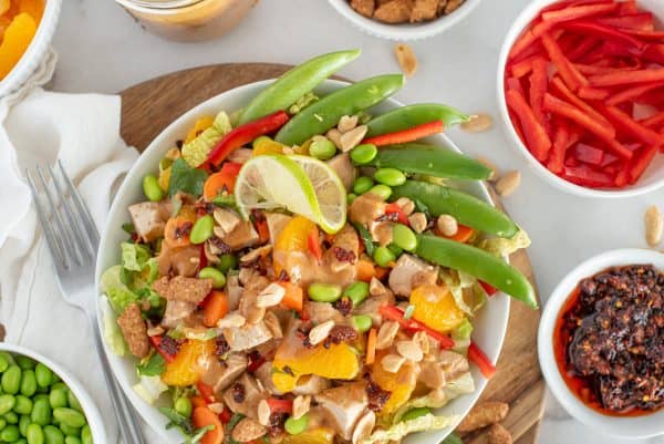 Asian chicken salad with bell peppers, chicken, oranges, and pea pods in a white bowl