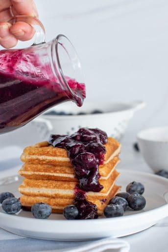 waffles with blueberry syrup being poured on top on a white plate