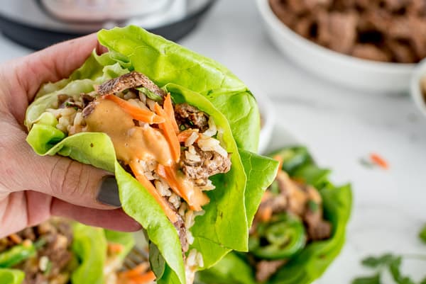 sliced steak with lettuce wraps, chopped carrots and peanut sauce in a hand
